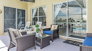 Eine sonnendurchflutete Terrasse mit Korbmöbeln, einem Glastisch und Blick auf Pool und Essbereich.