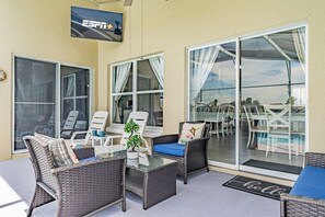 A sunlit patio with wicker furniture, a glass table, and a view of the pool and dining area. - 3BR Villa with Pool Spa and Games Room (Kissimmee)