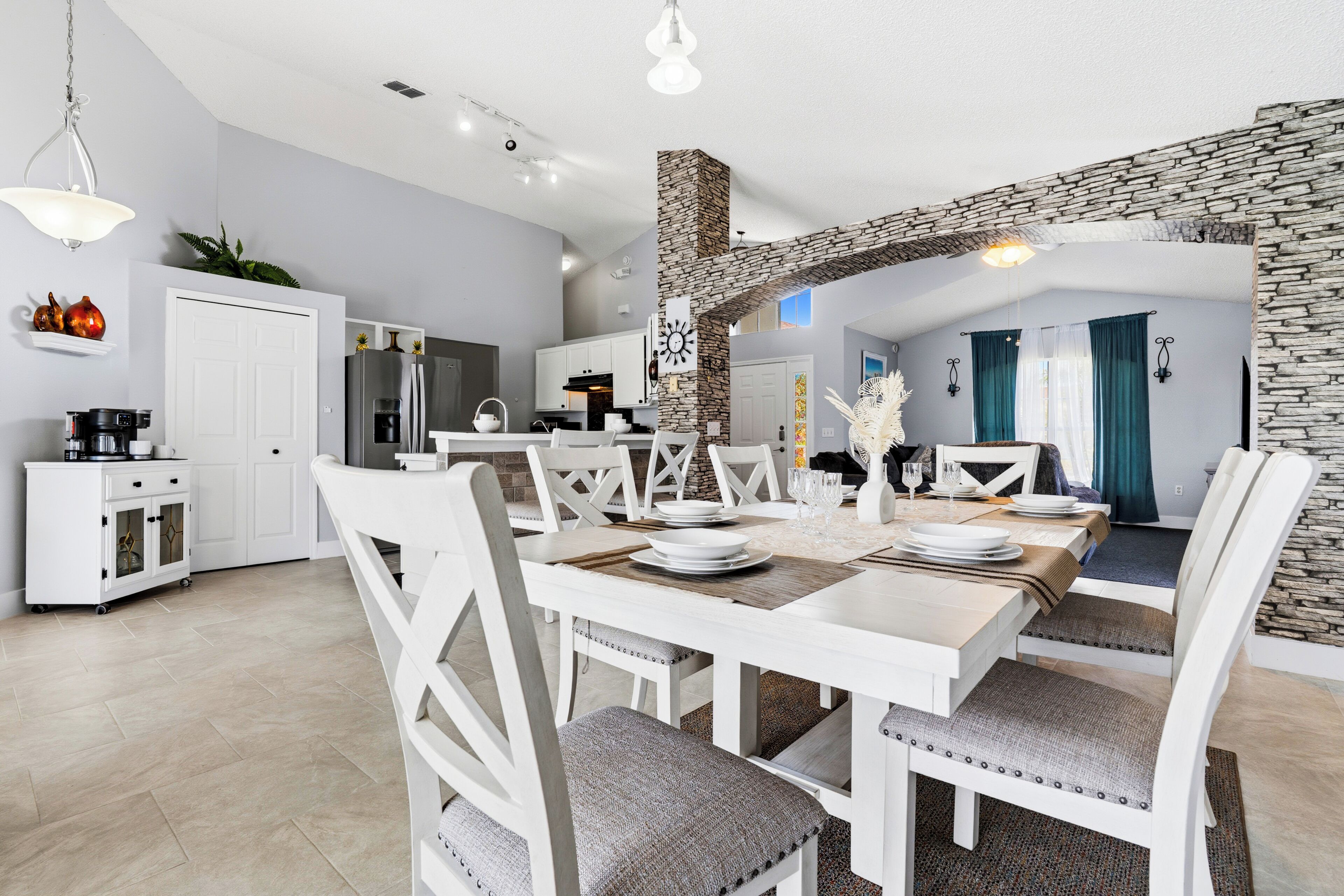 A modern kitchen with white cabinetry, a stone accent wall, and a dining area with white furniture.