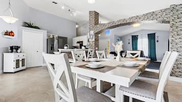 A modern kitchen with white cabinetry, a stone accent wall, and a dining area with white furniture.