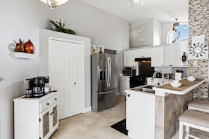 Una cocina moderna con muebles blancos, un refrigerador de acero inoxidable, un microondas y una pared de acento de piedra.