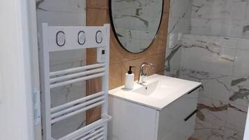 A bathroom with a white vanity, a mirror, a towel rack, and a shower.