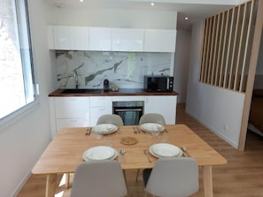 A modern kitchen with white cabinets, a marble backsplash, and a wooden dining table set for four.