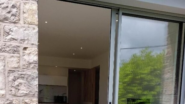 Un intérieur moderne avec un mur en pierre, une porte-fenêtre coulissante donnant sur un balcon et un coin repas avec une table et des chaises.