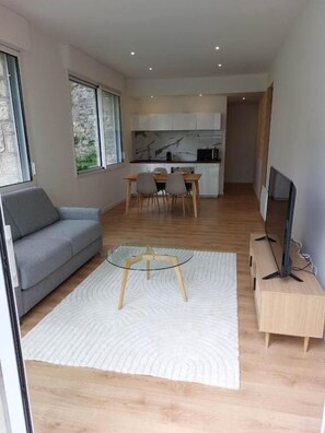 A modern living room with a sofa, a glass coffee table, and a TV stand. - Le Bompard 48m2 (Rodez)
