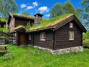 Puinen mökki, jossa on kivinen savupiippu, olkikatto ja kivestä rakennettu perustus.