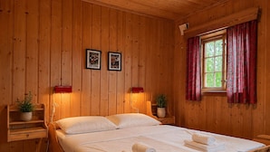 A wooden-paneled room with a bed, two framed pictures on the wall, a window with red curtains, and a small plant on a nightstand. - Mountain cabin 4 in Ål with sauna (Ål)