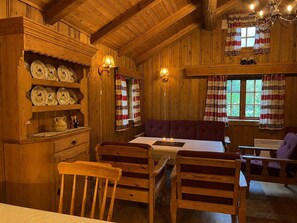 Un interior de fusta amb una taula de dinar, cadires, una banca i una estant amb plats de ceràmica.