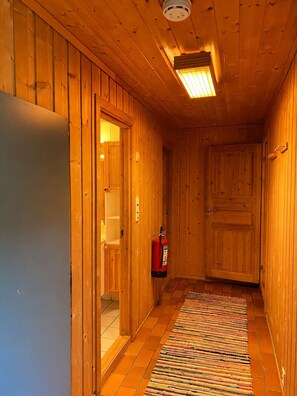 A wooden hallway with a fire extinguisher, a door, and a ceiling light fixture.