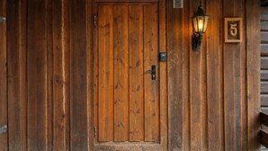 Une porte en bois avec une plaque portant le numéro « 5 », un interphone et un luminaire fixé au mur.