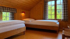 Une chambre dans un chalet en bois, avec deux lits, une fenêtre ornée de rideaux à carreaux et une chaise.