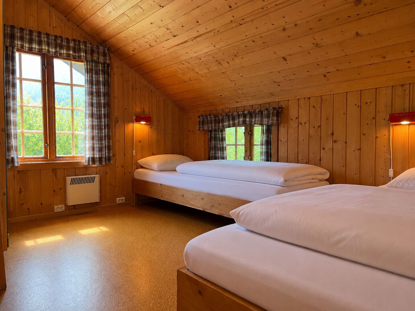 Una stanza in una baita di legno con due letti, una finestra e un termosifone a parete.