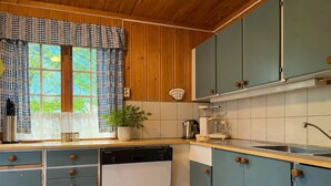 Une cuisine avec des meubles en bois, un lave-vaisselle, un évier et une fenêtre agrémentée de rideaux à motifs.