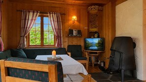 En mysig stuga med träpanel i taket, en öppen spis, en tv och ett fönster med gardiner.