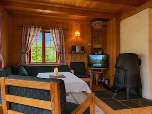 A cozy cabin interior with a wooden ceiling, a fireplace, a television, and a window with curtains.