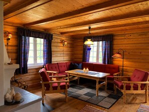 Interior acollidor d'una cabana amb sostre de fusta, cortines de quadres, un sofà vermell, una taula de fusta amb espelmes i un moqueta amb dibuixos.