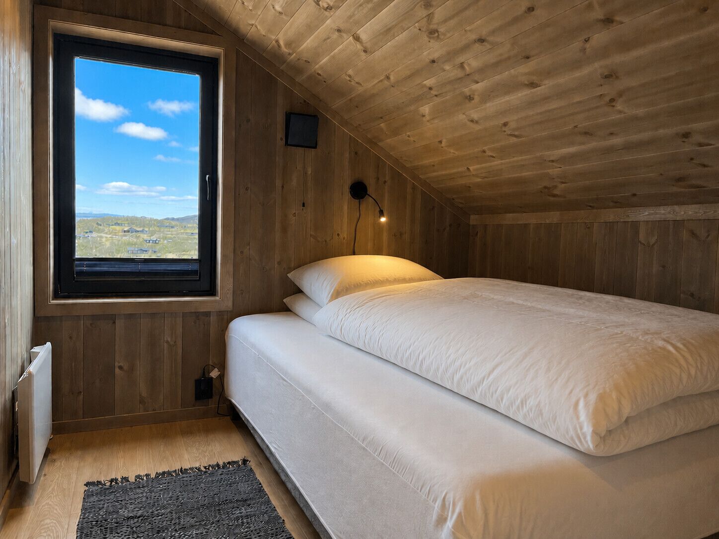Una stanza con un letto, una finestra vista, una lampada a parete e un termosifone.