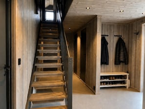 A wooden staircase leading to a hallway with a bench and shoe rack.