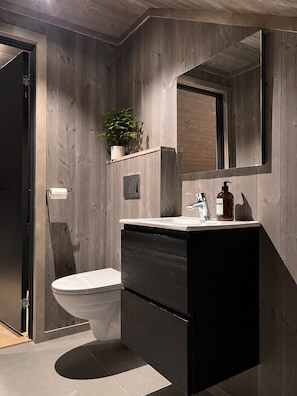 A modern bathroom with a wooden wall design, a toilet, a sink with a mirror, and a plant on the wall. - New spacious mountain cabin with sauna, Geilo (Hol)