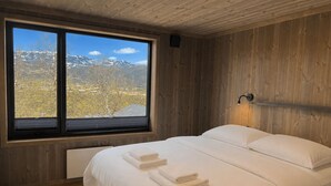 A bedroom with a large window, wooden walls, a bed with white linens, and a wall-mounted light fixture. - New spacious mountain cabin with sauna, Geilo (Hol)