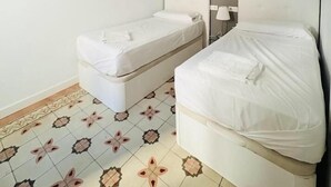 A room with two beds, a white wall, a gray accent wall, and patterned floor tiles.