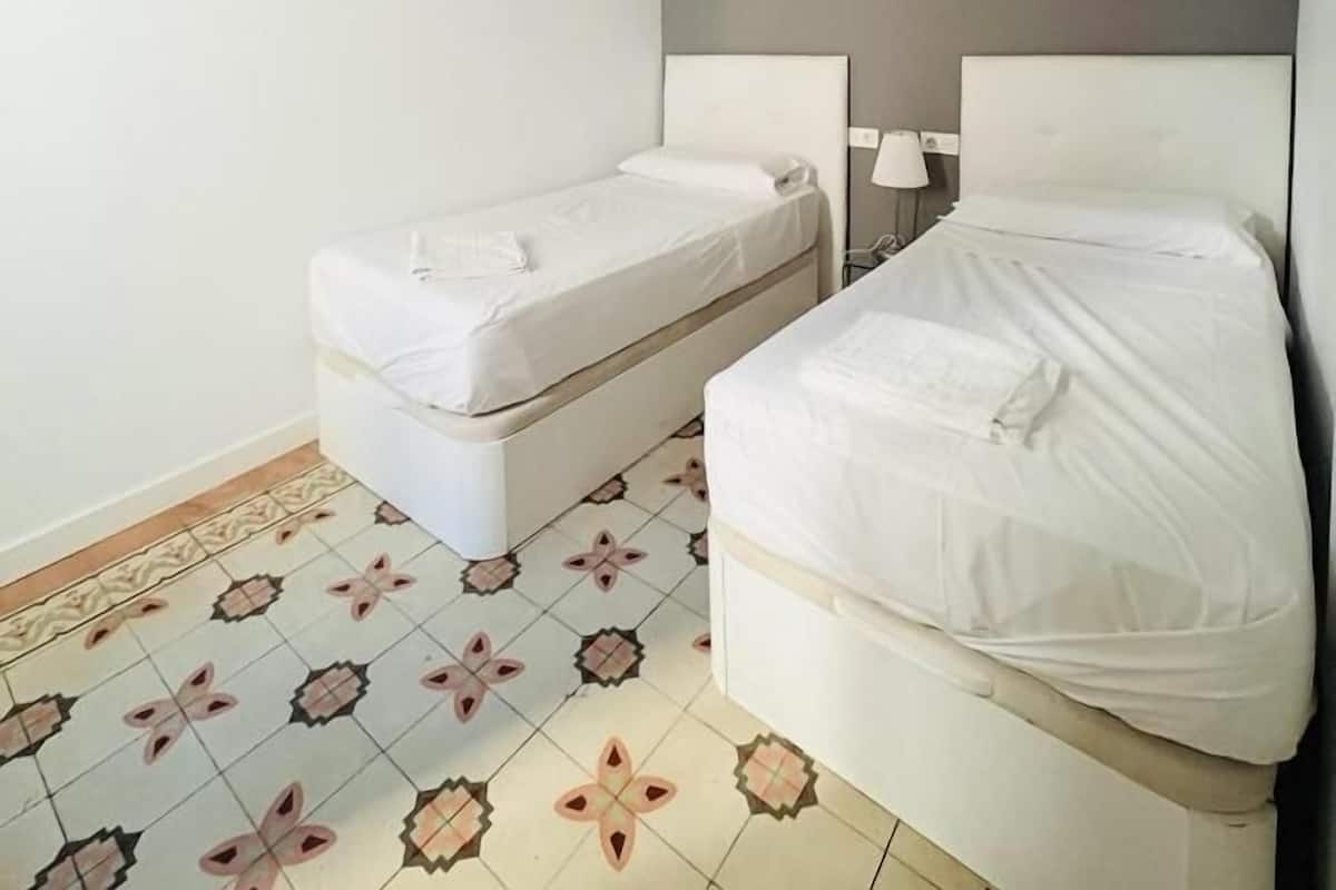 A room with two beds, a white wall, a gray accent wall, and patterned floor tiles.