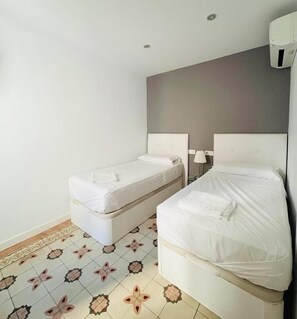 A room with two beds, a white wall, a gray accent wall, and patterned floor tiles.
