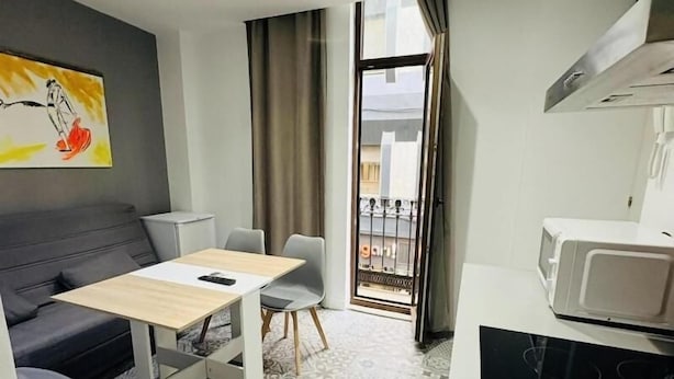 Un espacio habitable compacto con sofá, mesa de comedor, sillas, microondas y piso con diseño.