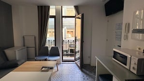 Habitación de hotel con sofá, sillas, mesa de comedor, microondas, televisión y balcón con vistas.