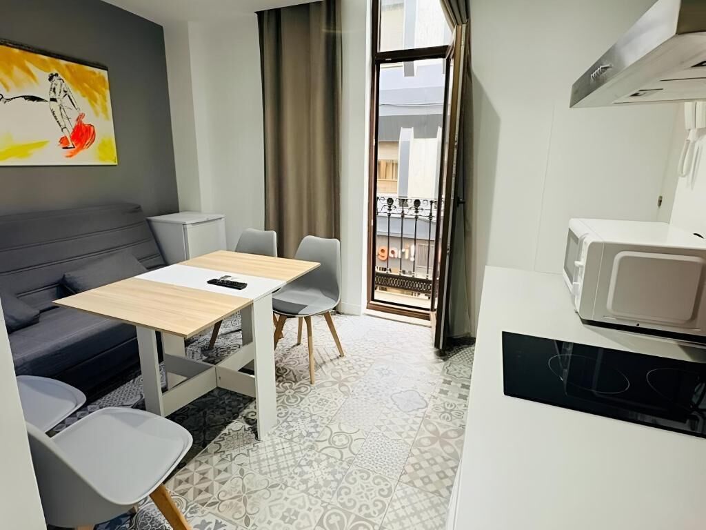 A compact living space with a sofa, a small dining table, a microwave, and a balcony with a view.