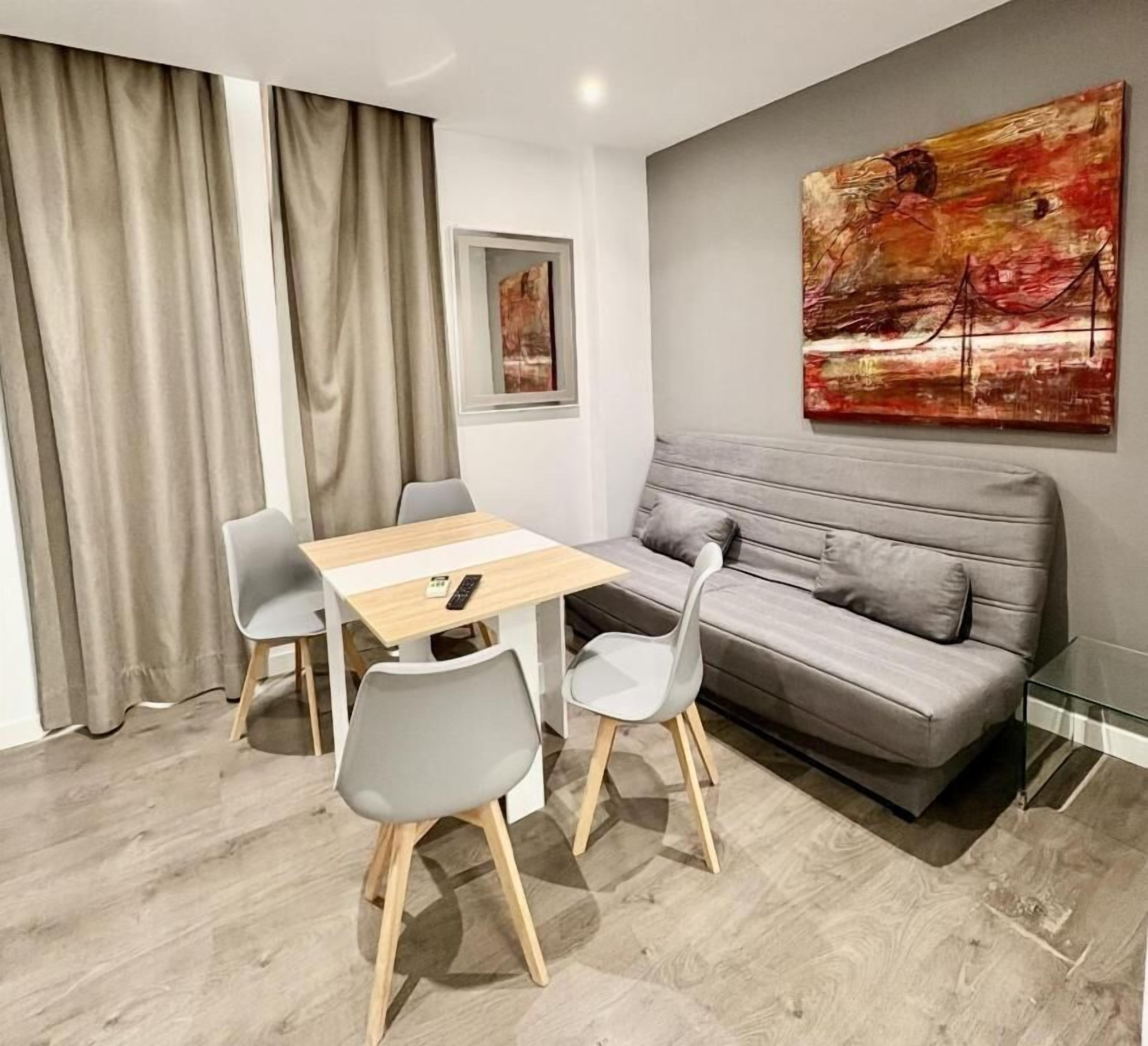 Ett modernt vardagsrum med en grå soffa, ett matbord i trä med fyra stolar och en stor, abstrakt tavla på väggen.