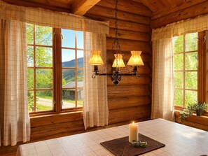 A cozy room with wooden walls, a large window with curtains, a table with a candle, and a hanging light fixture.
