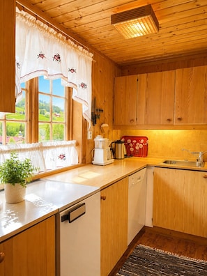 A kitchen with wooden cabinets, a window with floral curtains, a coffee maker, and a sink.