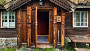 En rustik timmerstuga med en stor huvudentré, en liten veranda och en grund av sten.