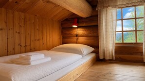 En stuga med träpanel, ett rum med en säng, ett fönster med gardiner och en väggmonterad lampa.