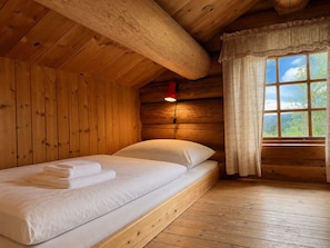 A wooden cabin room with a bed, a window with curtains, and a wall-mounted light.
