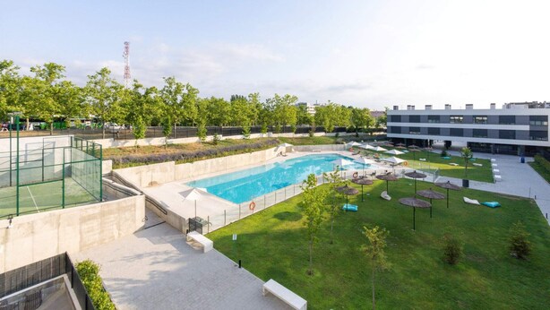 Una piscina con un'area verde, sdraio e un edificio moderno sullo sfondo.