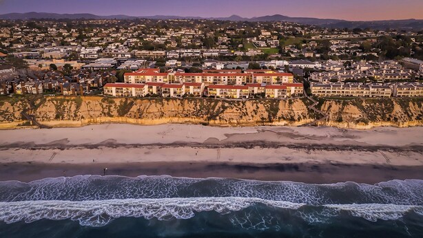 Un pueblo costero con un hotel destacado que cuenta con varios balcones con vistas a la playa.