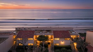 Un hotel frente a la playa con varias edificaciones, piscina y vista al océano.