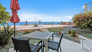 Un patio con una mesa y sillas, un paraguas rojo y vista a la playa y al océano.