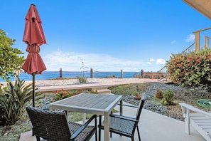 Eine Terrasse mit Tisch und Stühlen, einem roten Sonnenschirm und Blick auf Strand und Meer.