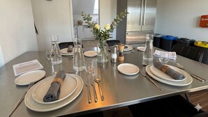 Una mesa de comedor dispuesta con platos, cubiertos, vasos y un florero con flores.
