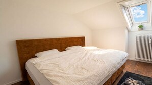 Una cama bien hecha con cabecera de madera en una habitación con techo inclinado y ventana con vista al cielo.
