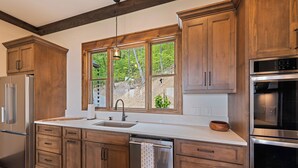 Una cucina con mobili in legno, un frigorifero in acciaio inossidabile, una lavastoviglie e un'ampia finestra vista su un'area verde.