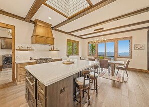 A spacious kitchen with a large island, wooden beams, and a view of mountains through large windows. - Gold Rain Retreat Newly Built! 4BD,3.5 BA in Smoky Mountain Retreat (Maggie Valley)