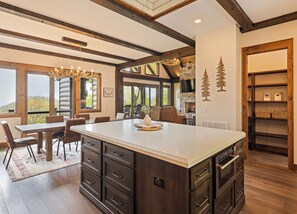 A spacious kitchen with a large island, wooden beams, stone fireplace, and a dining area with a view. - Gold Rain Retreat Newly Built! 4BD,3.5 BA in Smoky Mountain Retreat (Maggie Valley)