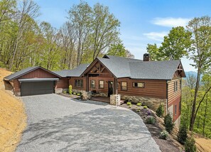 A log cabin with a garage, stone foundation, and a gravel driveway. - Gold Rain Retreat Newly Built! 4BD,3.5 BA in Smoky Mountain Retreat (Maggie Valley)