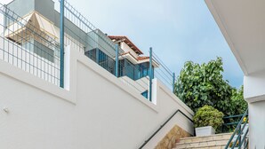 Uma escadaria de pedra leva a uma varanda com paredes brancas, corrimão e plantas em vasos.