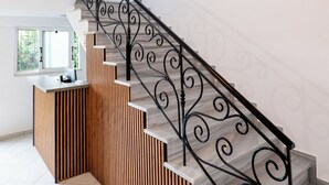 Uma escadaria moderna com acabamento em madeira e guarda-corpos de metal, que leva a uma área de recepção com balcão e luminária pendente.