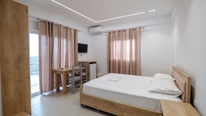 Quarto com cama de madeira, uma escrivaninha, uma cadeira e uma televisão.